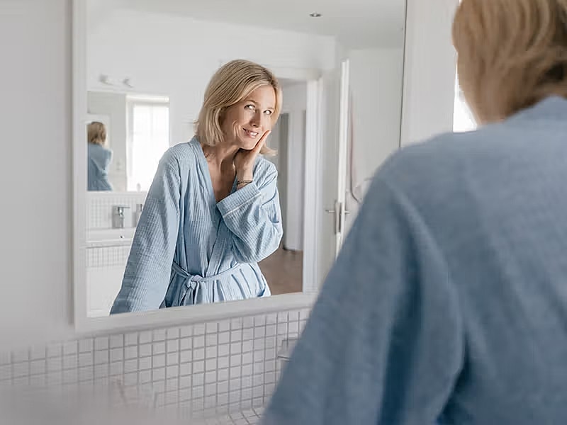 Woman smiling in mirror, wearing blue robe.